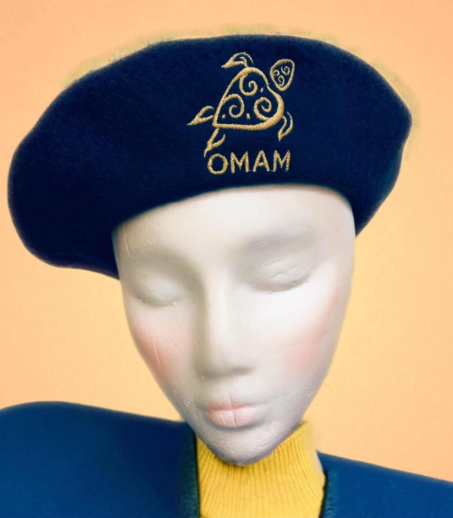 Teal blue beret with OMAM turtle logo embroidered in gold thread.