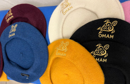 Collection of berets in various colors with 'OMAM' branding gold embroidered turtle logo.